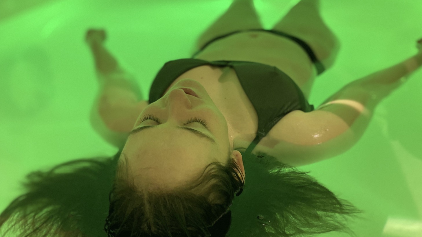 A floater resting with eyes closed in green-lit water