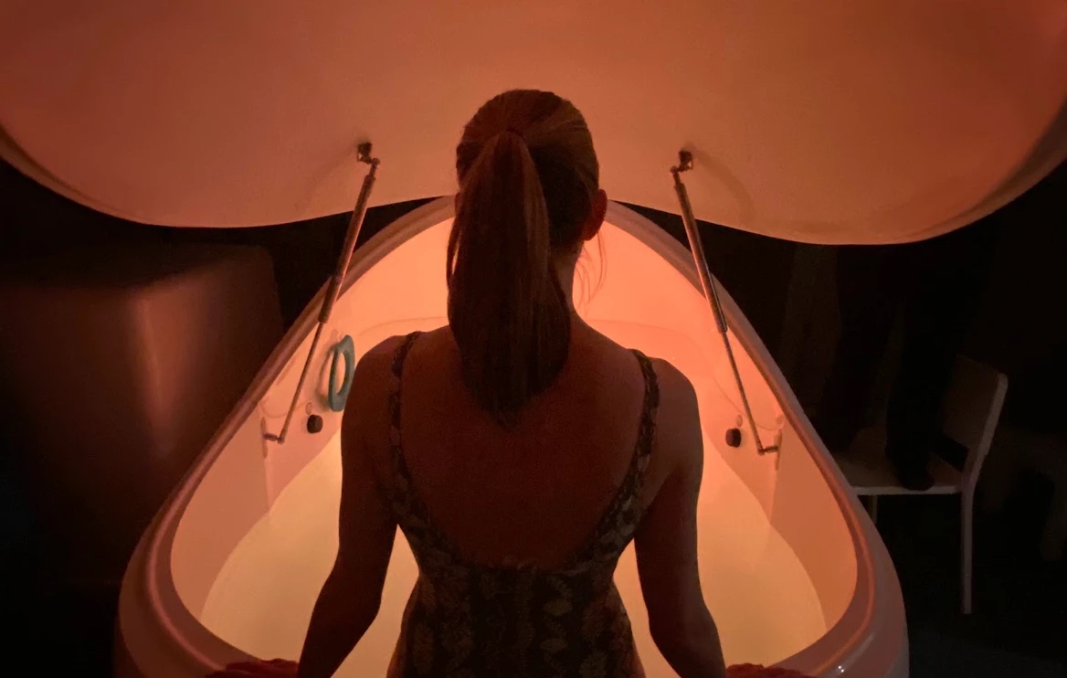 A guest stepping into the warmly lit floatation pod at Floatwell Cambridge