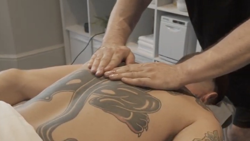A therapist's hands working across a client's back in the treatment room