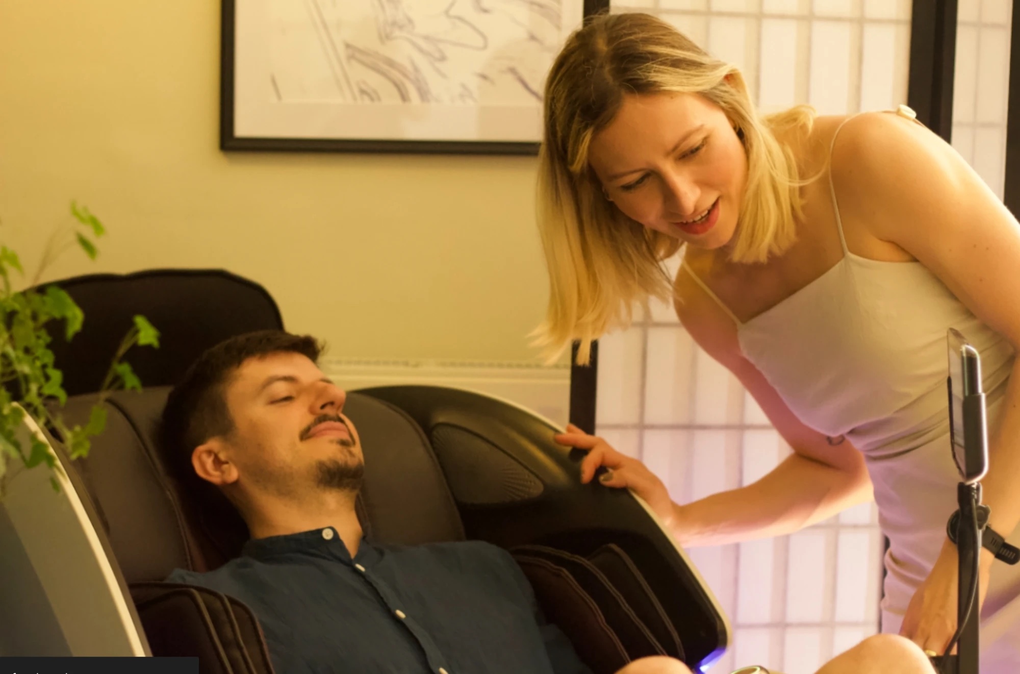 A guest settling into the AI massage chair at Floatwell Cambridge, with a member of the team alongside