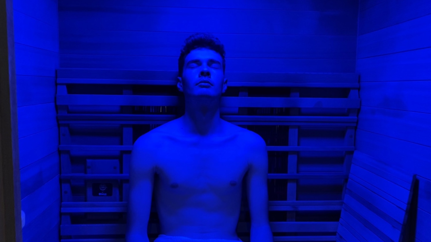 A guest sitting upright in the infrared sauna under cool blue light