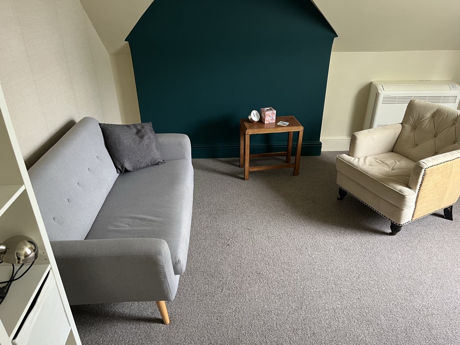 A room available for practitioner hire at Floatwell, with a sofa, an armchair and a side table against a deep green wall